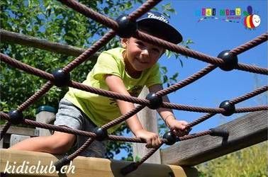 Ein kleiner Junge klettert auf einem Spielplatz über ein Seilnetz.
