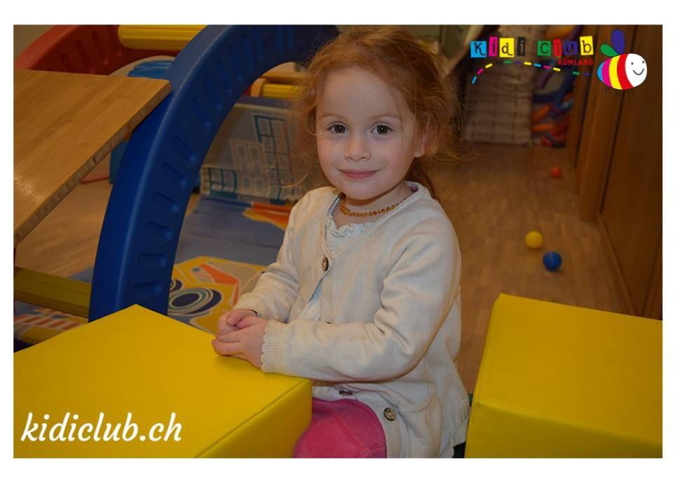 Ein kleines Mädchen sitzt auf einem gelben Klotz, in der Ecke steht die Website kidiclub.ch