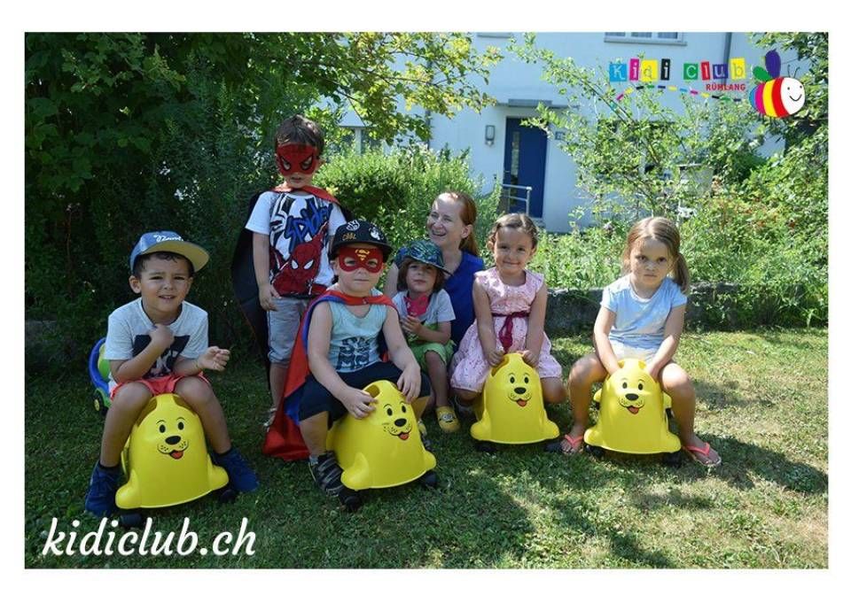 Eine Gruppe Kinder sitzt auf gelbem Spielzeug im Gras.