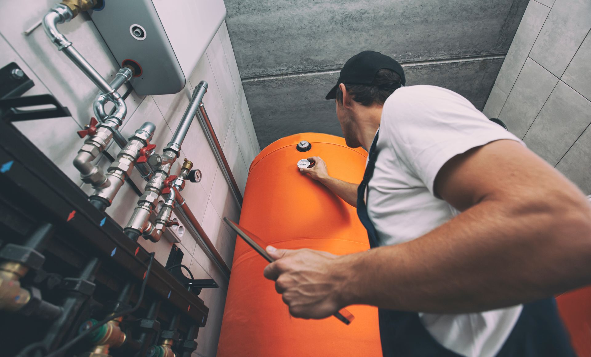 Ein Techniker inspiziert einen orangefarbenen Industrietank mit Rohren und Messgeräten in einem Maschinenraum.