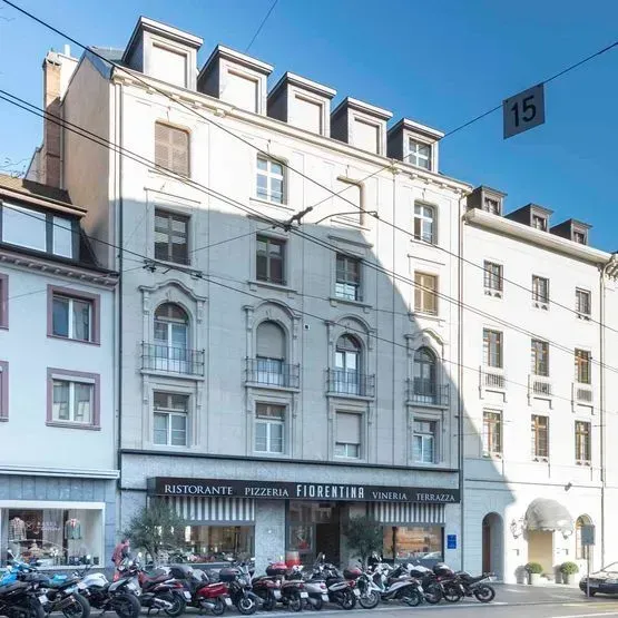 Straße mit hohen weißen Gebäuden, geparkten Rollern und einem Restaurant im Erdgeschoss unter blauem Himmel