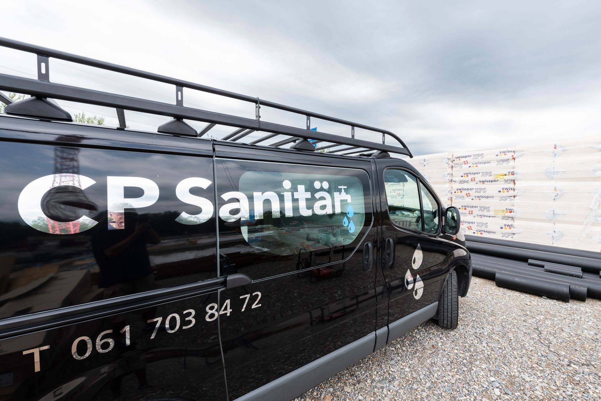 Firmenwagen der Firma CP Sanitär parkt im Freien neben einer Kiesfläche und einer mit Schildern bedeckten Mauer.