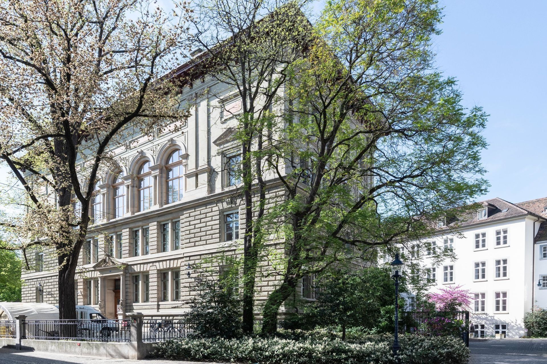 Eine von Bäumen gesäumte Straße mit einem historischen Steingebäude und einem geparkten Lieferwagen an einem sonnigen Tag
