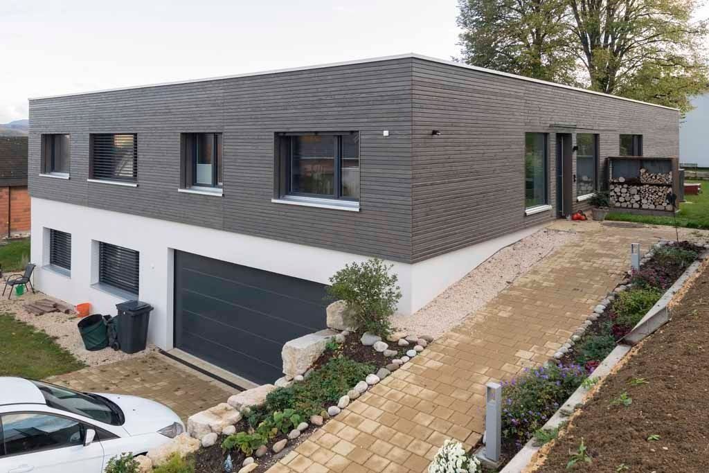 Modernes zweistöckiges Haus mit grauer Fassade, Garage und schräger Steinauffahrt in einem angelegten Garten