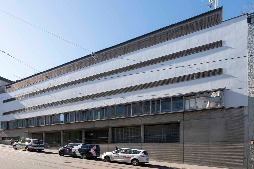 Modernes weißes Gebäude mit horizontalen Fenstern und geparkten Autos entlang der Straße