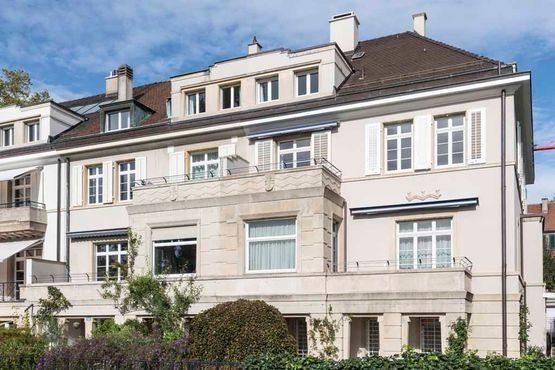 Großes weißes Wohnhaus mit Balkonen und Dachgauben unter blauem Himmel