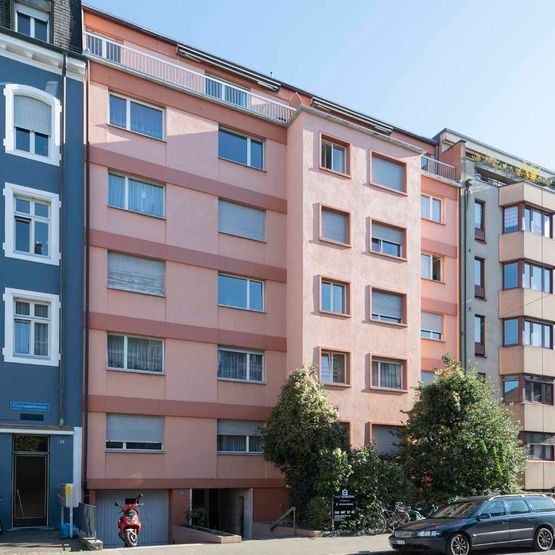 Pastellfarbenes Wohnhaus mit geparkten Autos und zwei Bäumen an einer sonnigen Straße