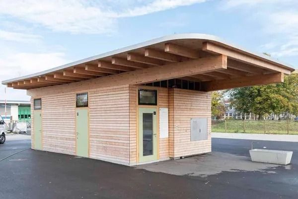 Kleines, modernes Holzgebäude mit breitem, weit überhängendem Dach auf einem gepflasterten Grundstück