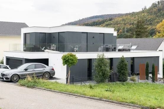 Modernes, weißes zweistöckiges Haus mit großen Fenstern, einem silbernen Auto und einem grasbewachsenen Vorgarten