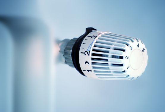 Nahaufnahme eines weißen Heizkörperthermostats, eingestellt auf Stufe 2, an einer blauen Wand.