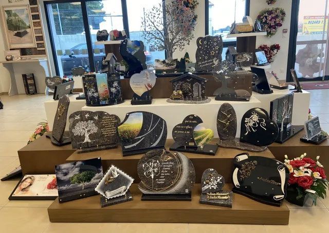 Exposition de diverses pierres commémoratives, dont beaucoup ornées de photos, à l'intérieur d'une boutique. Modèles en pierre brune, noire et blanche.