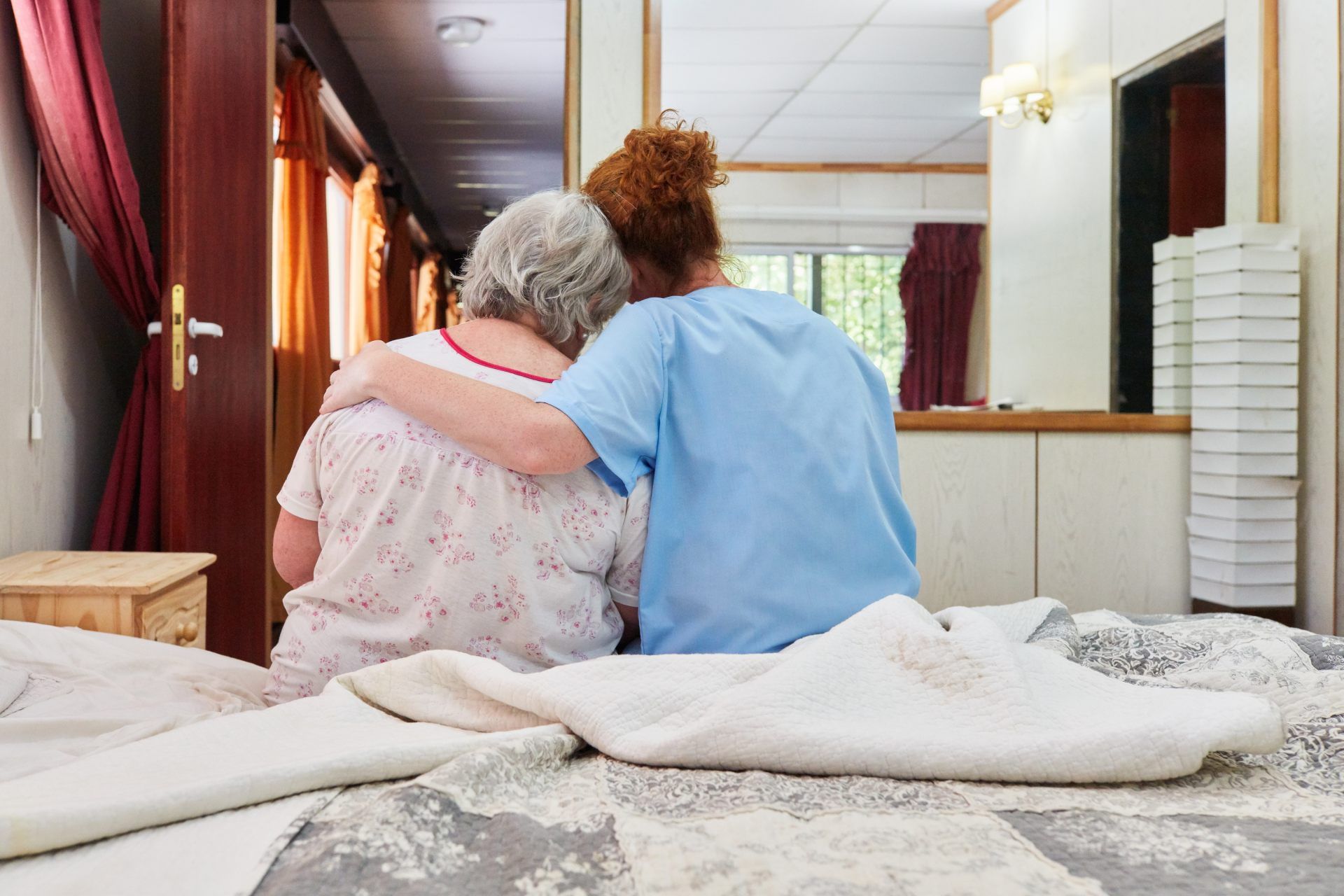 Eine Krankenschwester umarmt eine ältere Frau auf einem Bett