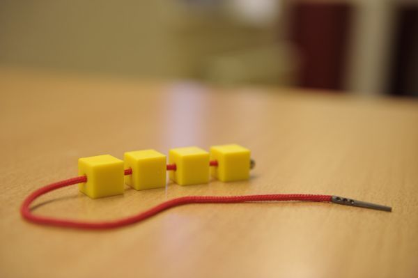 Roter Schnürsenkel mit vier gelben Würfeln, Fädelspiel