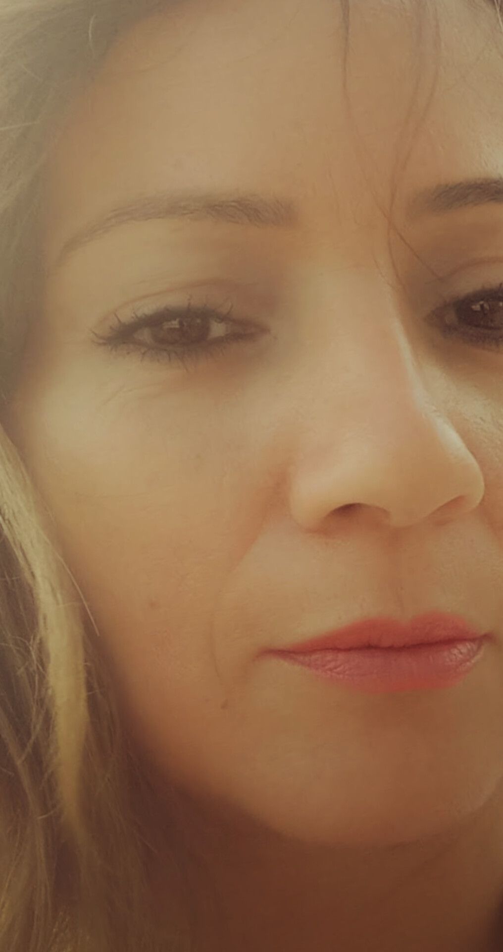 Primer plano del rostro de una mujer, mirando hacia abajo. Tiene piel clara, ojos marrones y lápiz labial color melocotón.