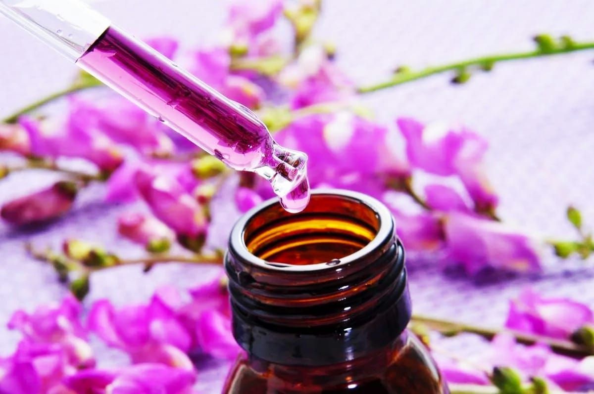 Se vierte un gotero en una botella con flores violetas en el fondo.