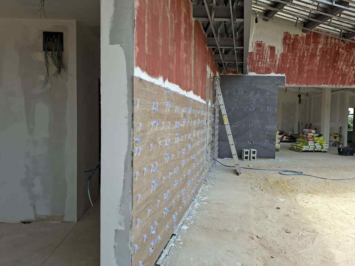 Obra en renovación con paredes sin terminar, cableado expuesto, escalera y materiales de construcción en el suelo.