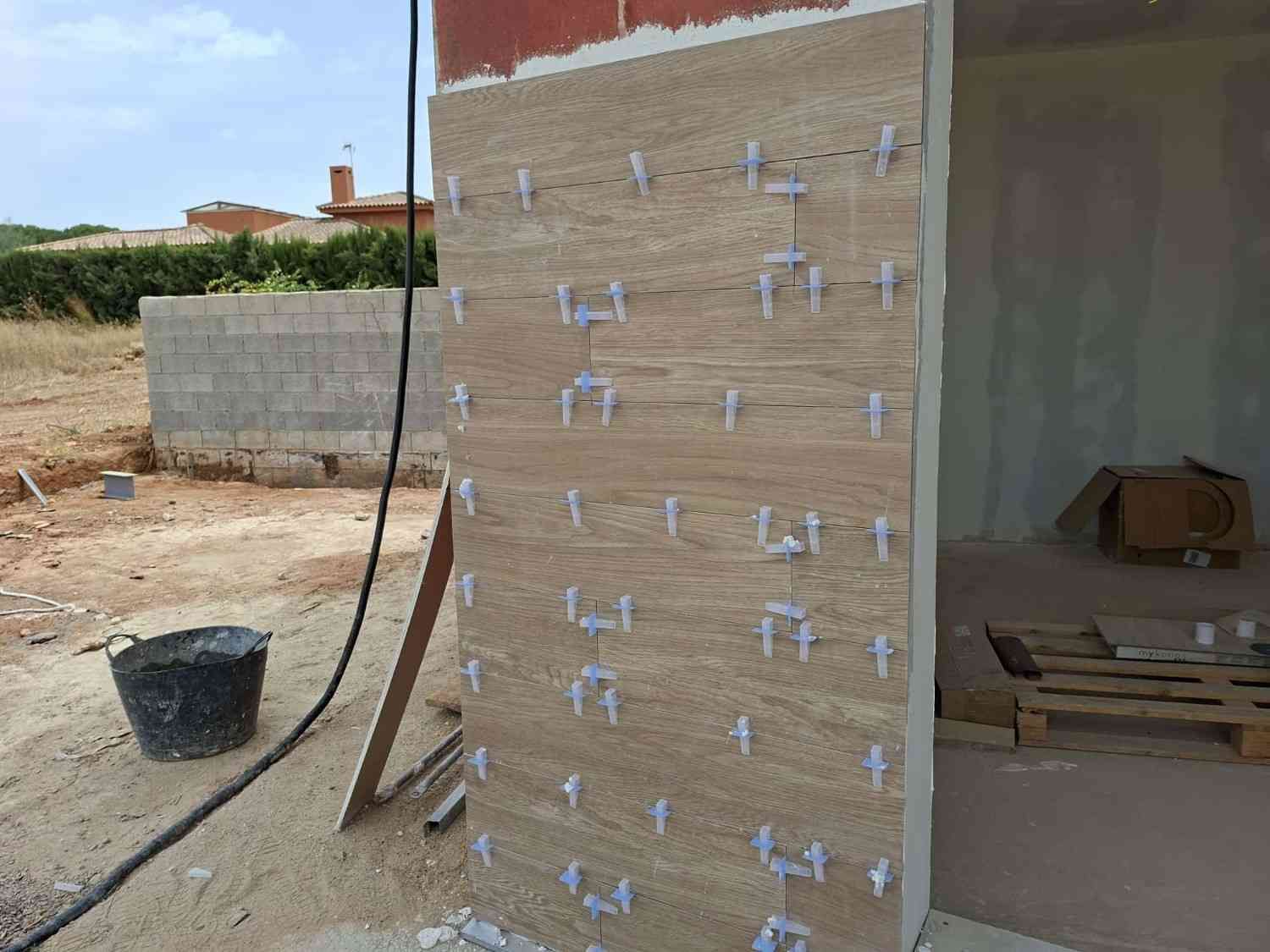 Muro de construcción parcialmente terminado con clips de montaje blancos junto a una puerta abierta en el exterior.