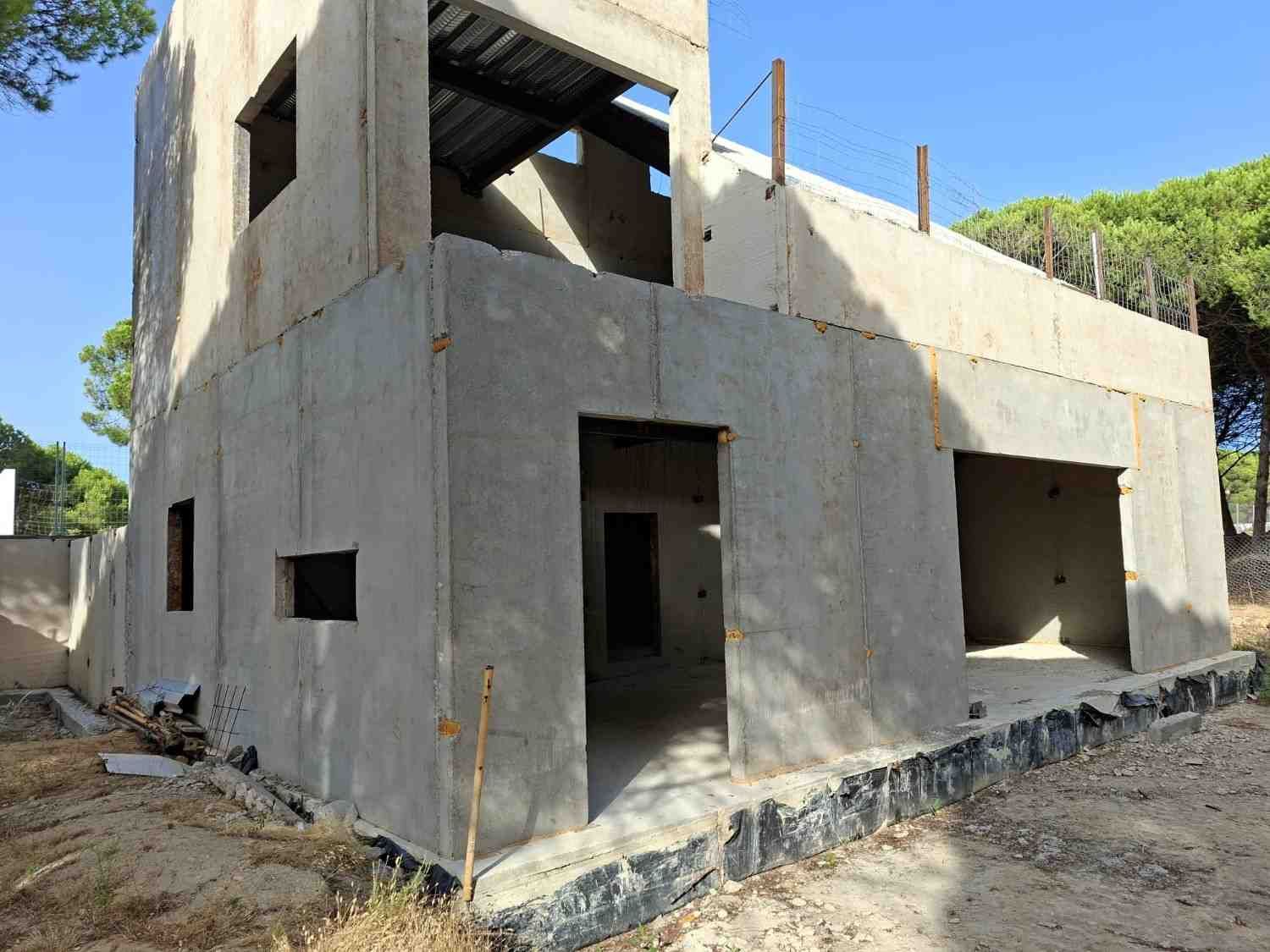 Casa de hormigón de dos plantas sin terminar en construcción, con puertas y ventanas abiertas en el exterior.