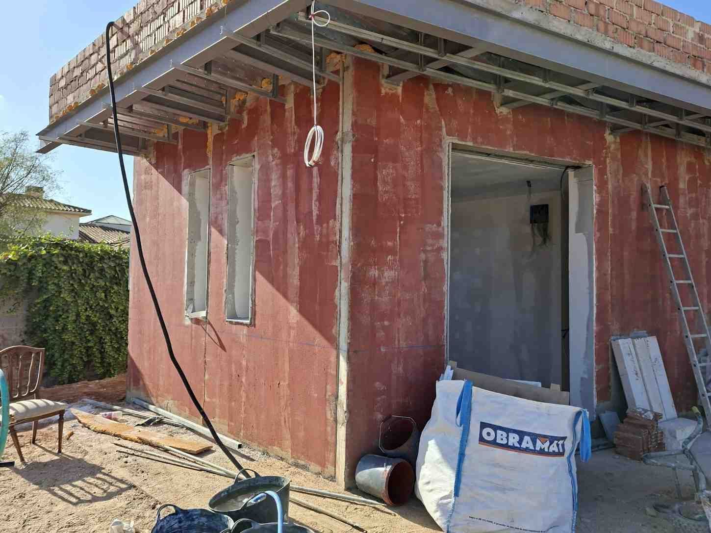 Exterior de una casa roja parcialmente construida con andamios, escalera y materiales de construcción en el exterior.