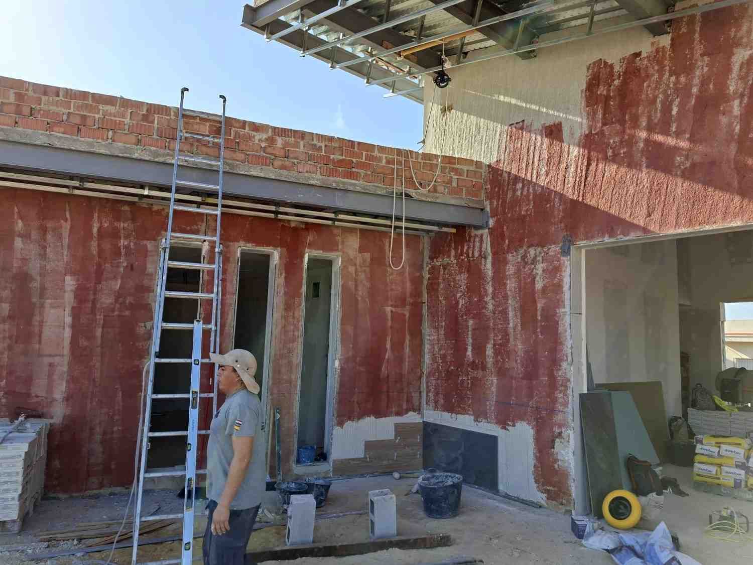 Obrero en una zona de construcción manchada de rojo con una escalera, cubos y una puerta abierta en reparación.