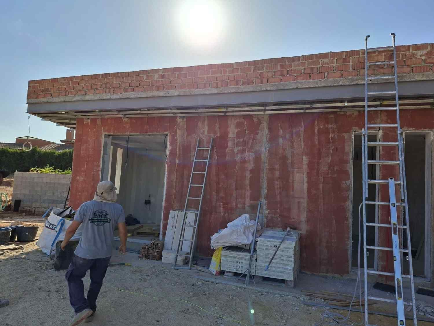 Dos trabajadores en un edificio de ladrillo rojo en construcción, con escaleras y materiales apilados en el exterior.
