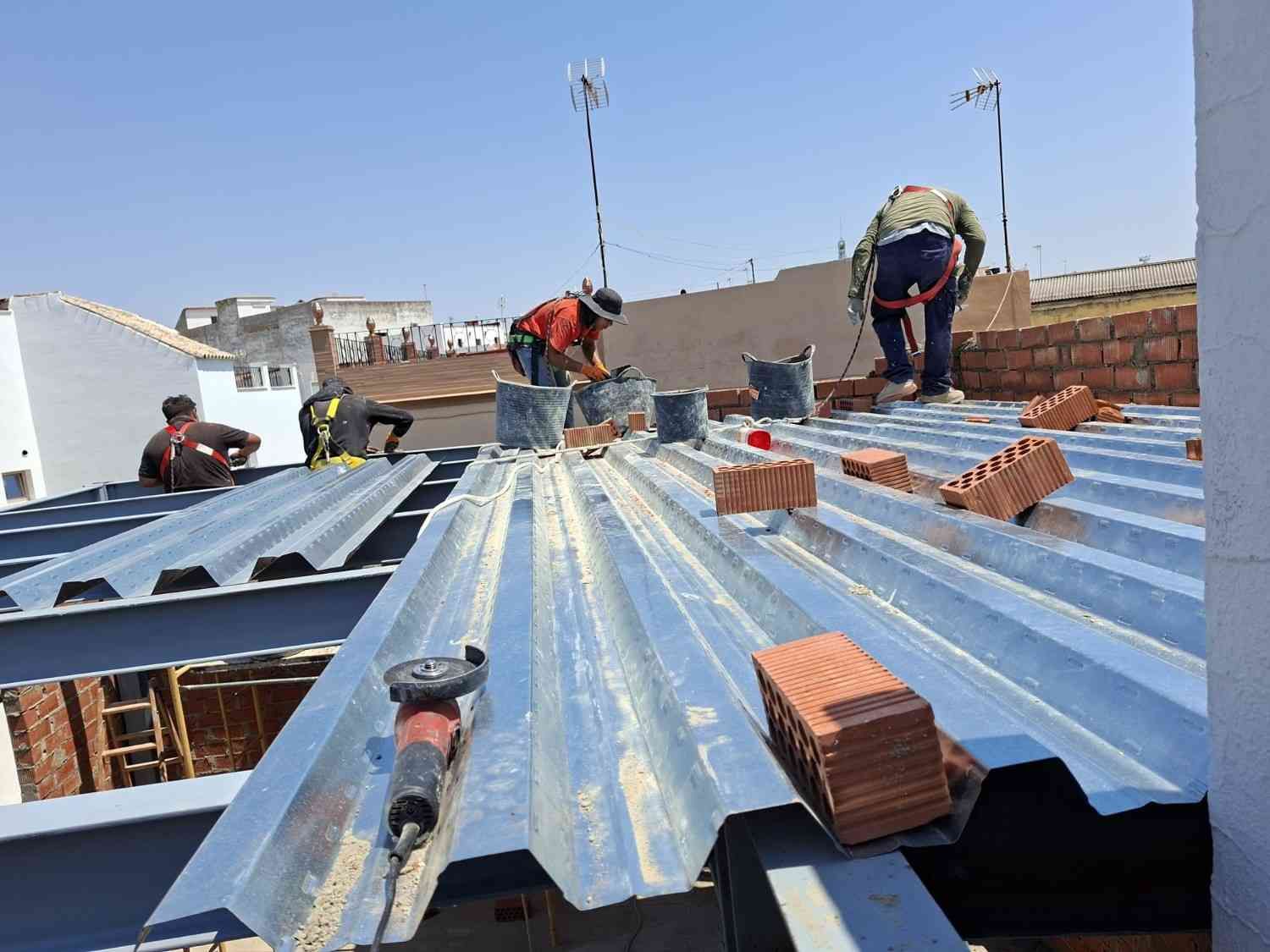 Trabajadores colocando techos de chapa ondulada con ladrillos encima en una obra de construcción.