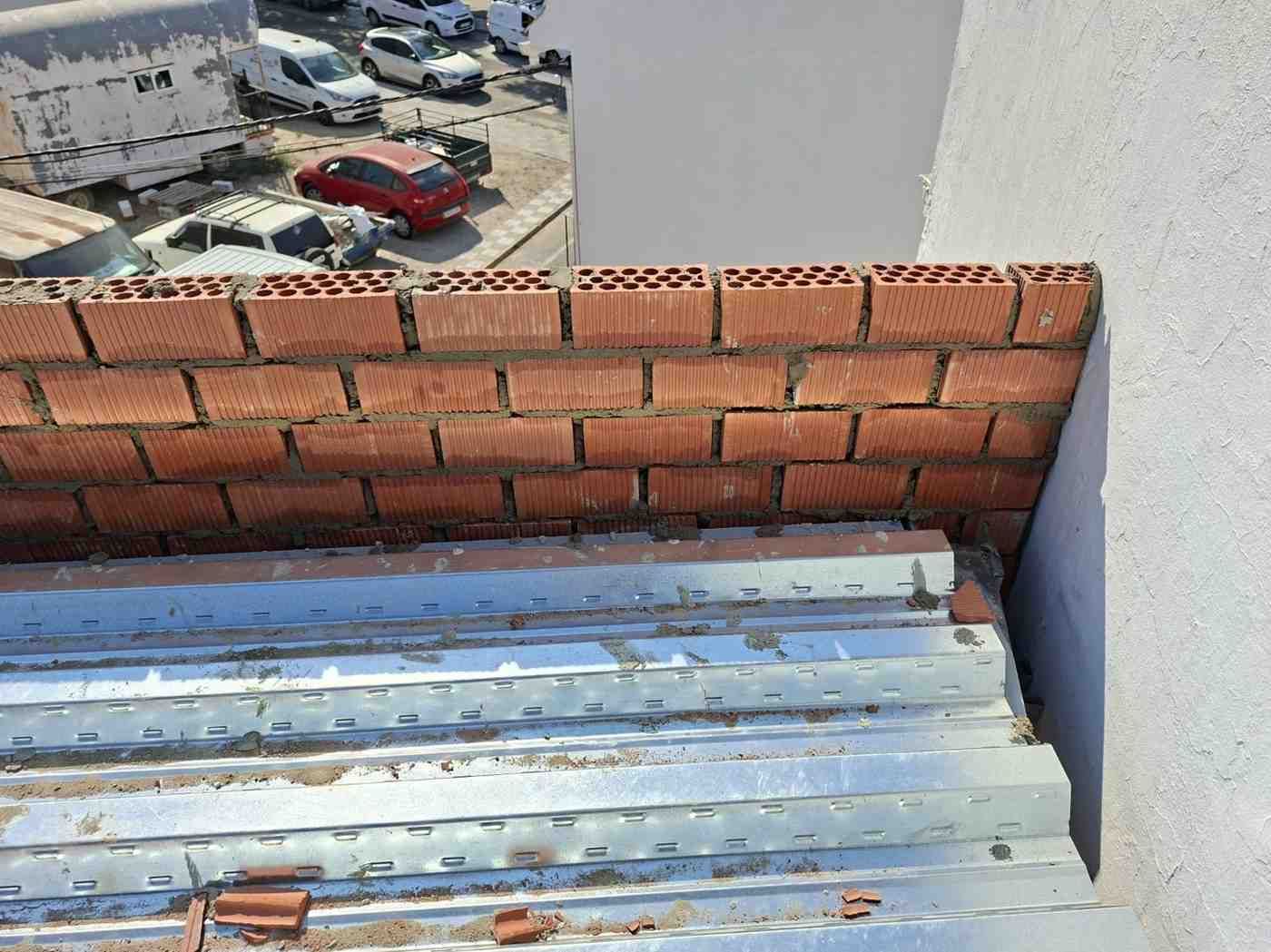 Vista desde la azotea con pared de ladrillo rojo, techo de chapa ondulada y coches aparcados al fondo.