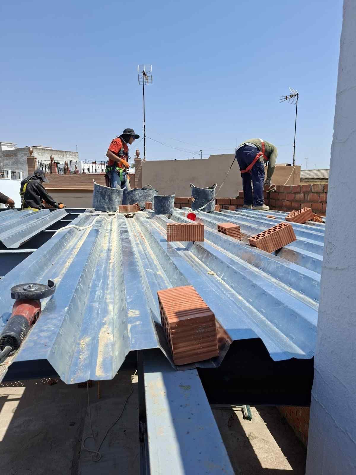 Trabajadores colocando ladrillos sobre un techo de chapa ondulada azul en una obra de construcción.