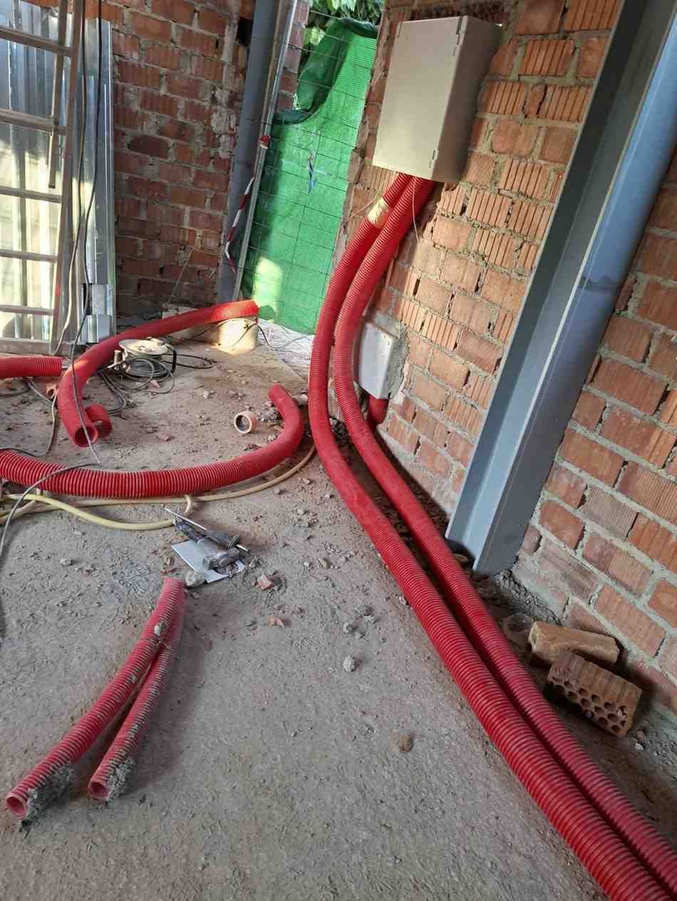 Conductos eléctricos rojos tendidos a lo largo de una pared de ladrillos en una polvorienta pasarela de construcción.