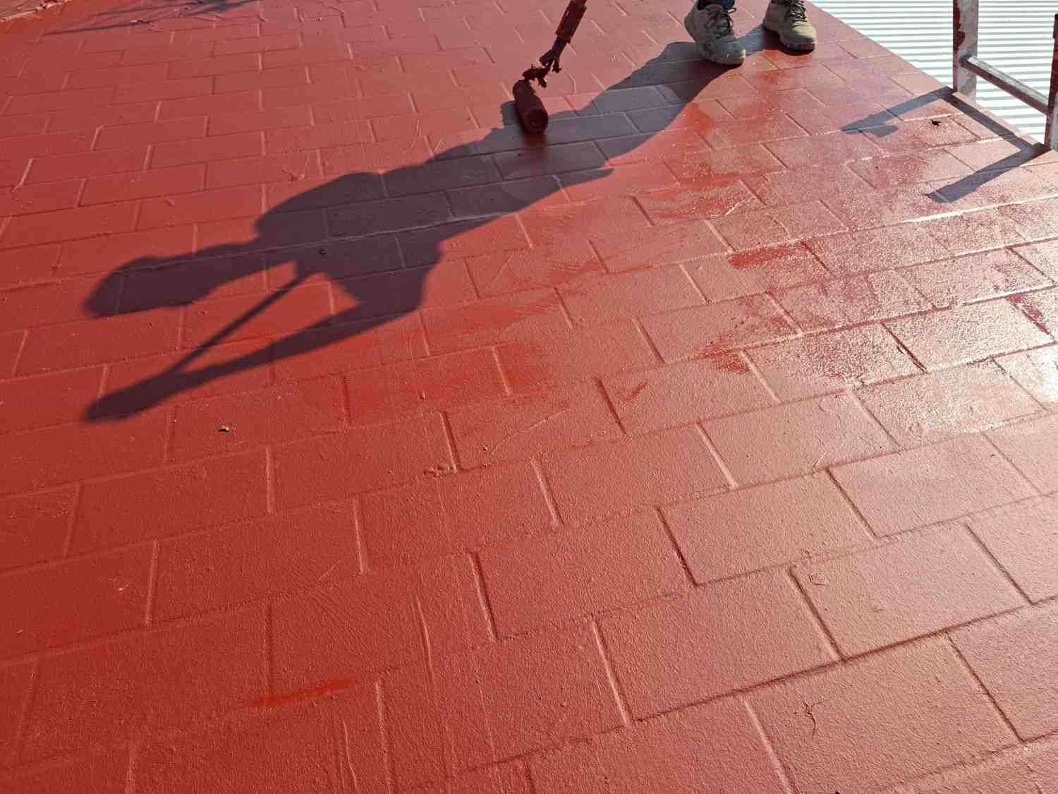 Sombras de dos personas caminando sobre un suelo de baldosas rojas bajo la luz del sol.