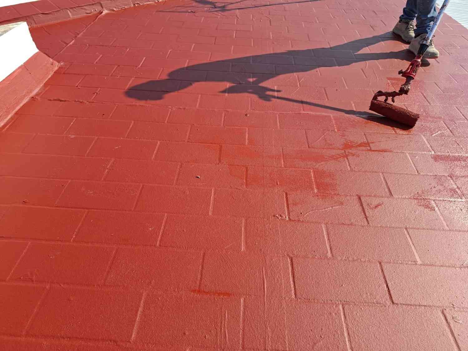 Trabajador pintando un tejado rojo con un rodillo.