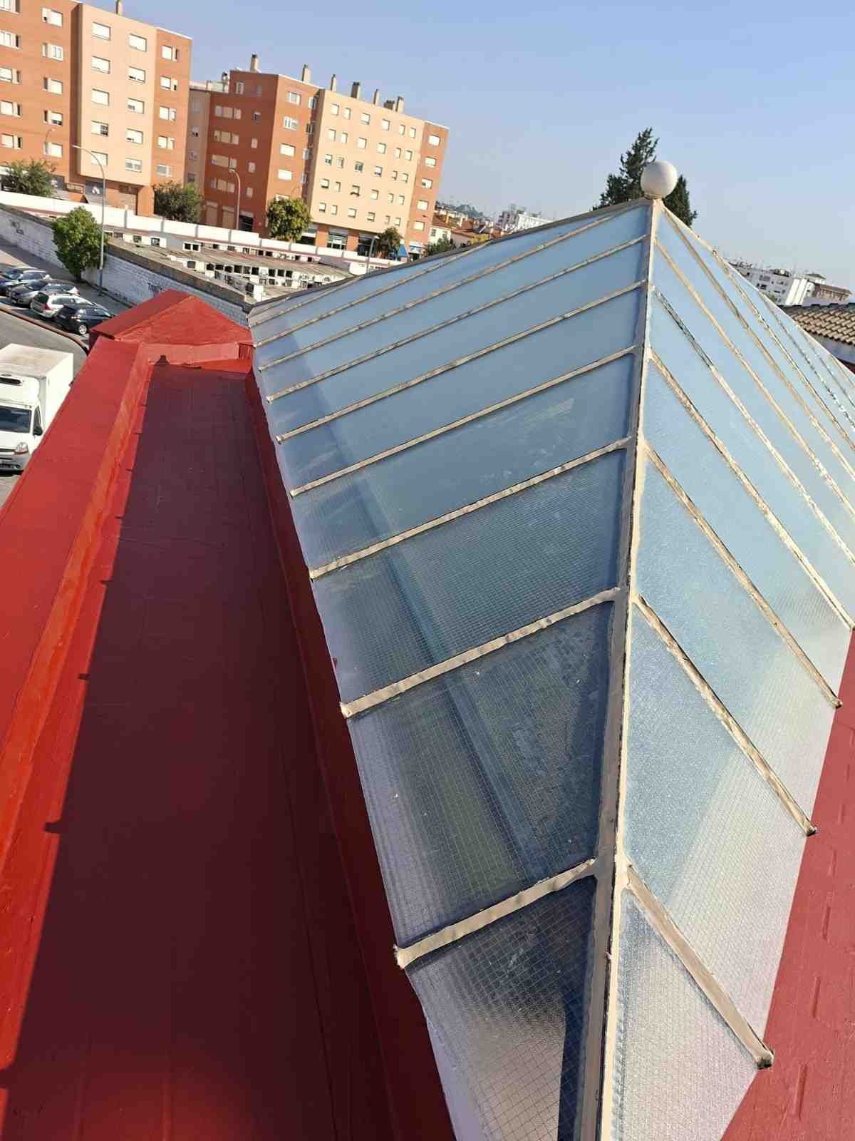 Vista desde la azotea de una claraboya de cristal rojo y azul con edificios de apartamentos al fondo.