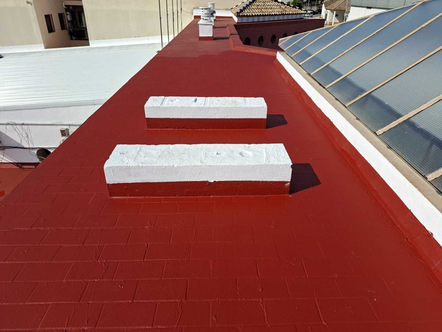 Techo plano rojo con dos rejillas de ventilación blancas junto a una hilera de paneles solares.