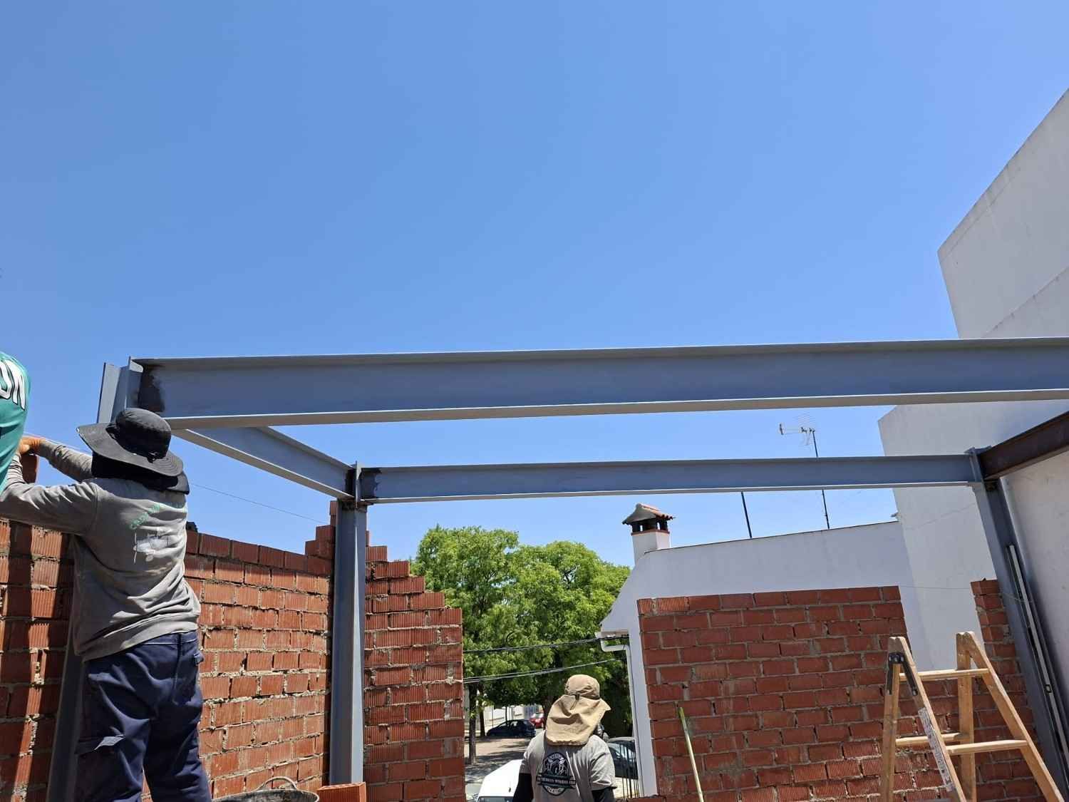 Dos trabajadores instalando una estructura metálica de techo en un edificio de ladrillo bajo un cielo azul despejado.