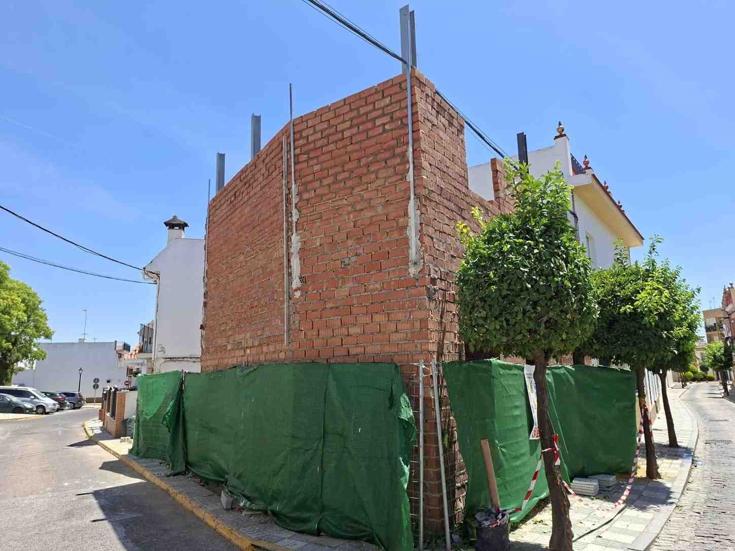 Edificio de ladrillo en construcción en una soleada esquina, envuelto en una red protectora verde.