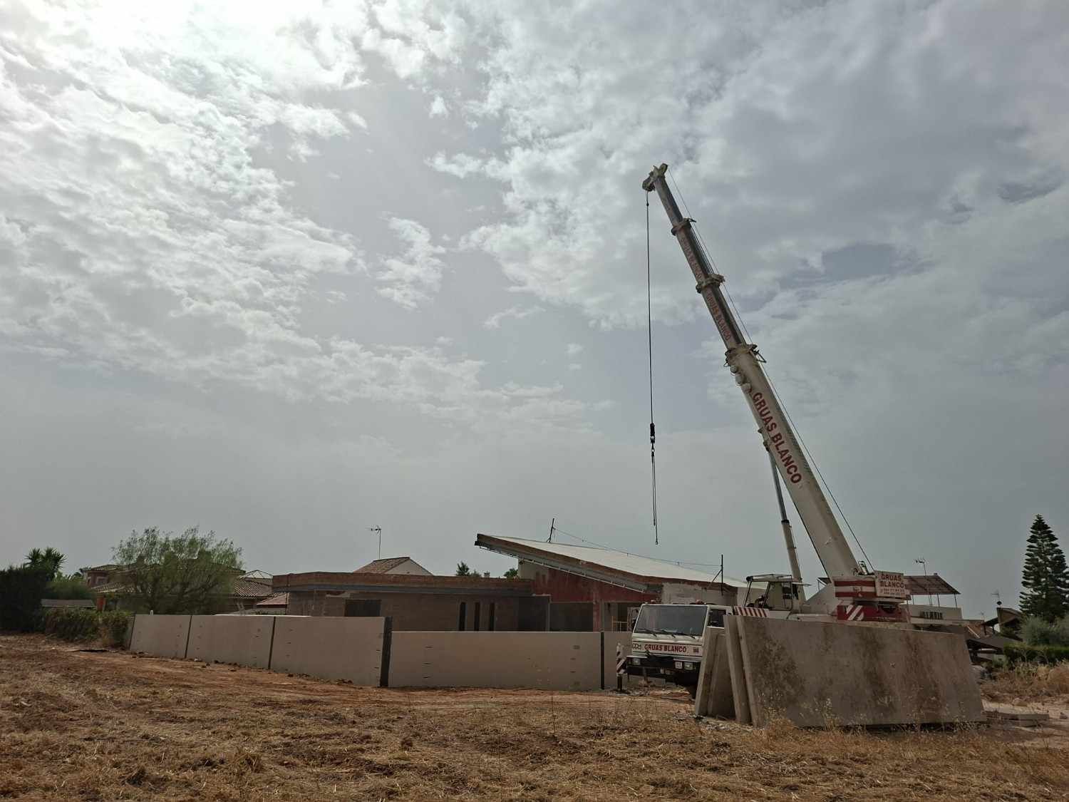 Una grúa de construcción está levantando material cerca de un edificio bajo un cielo nublado.