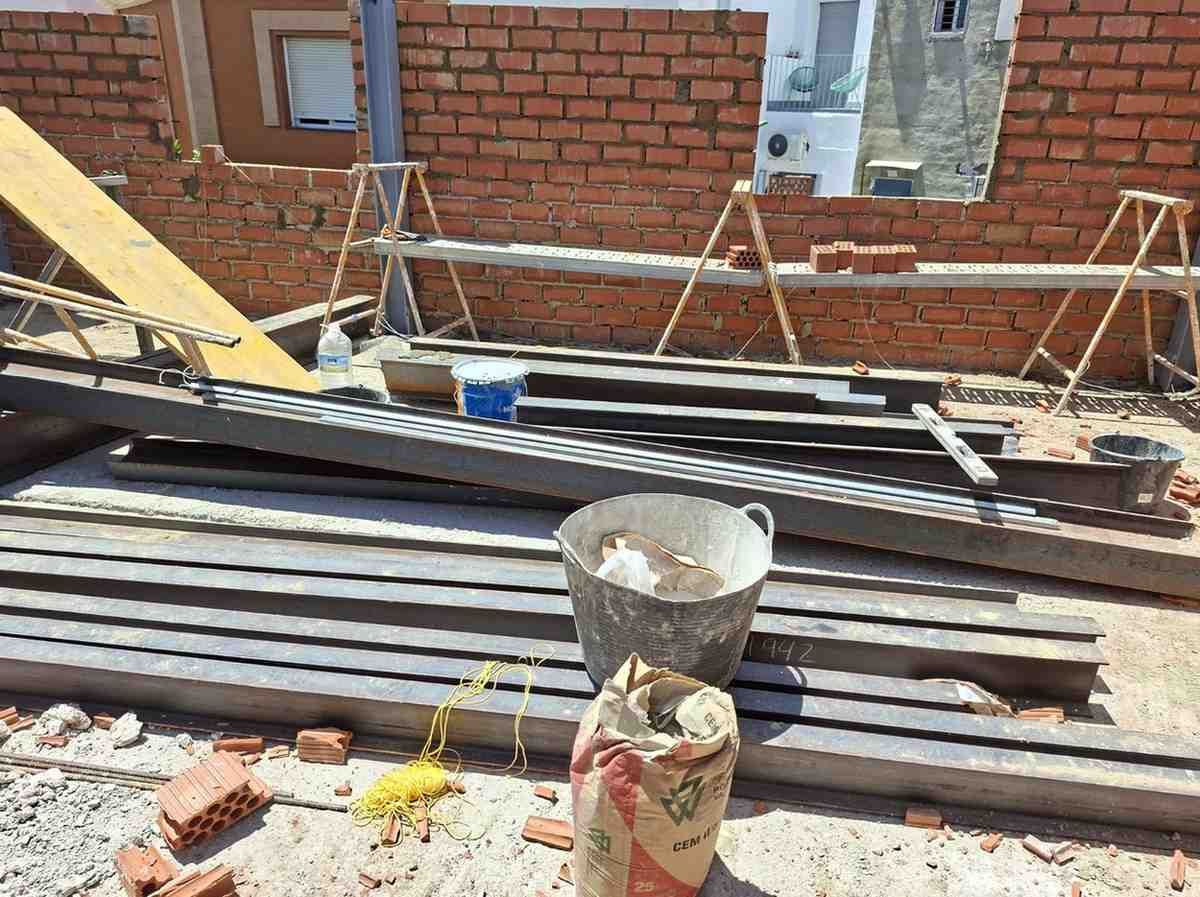 Obra en construcción con láminas de metal apiladas y herramientas frente a una pared de ladrillos.