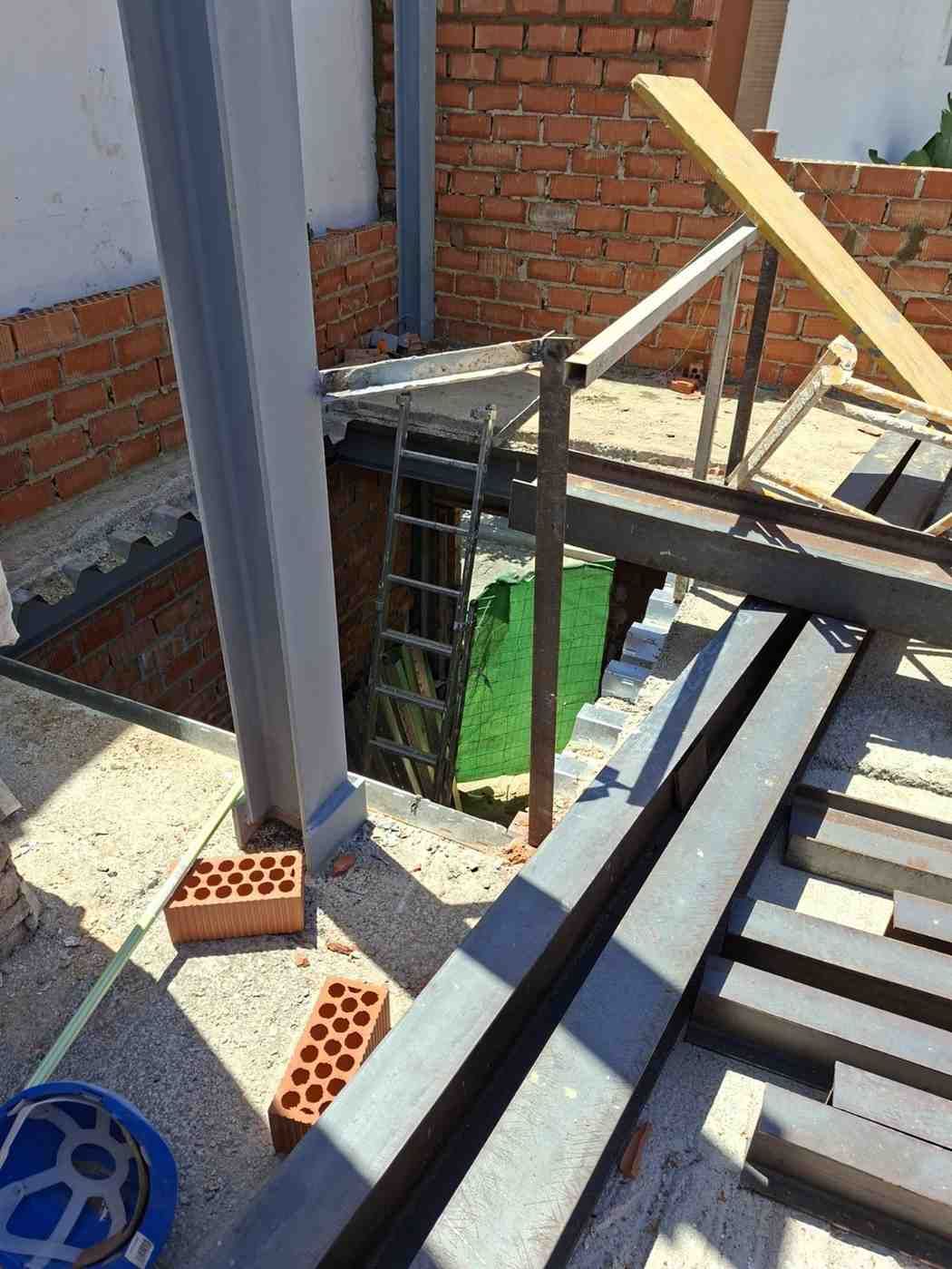 Obra en construcción con vigas de acero, muros de ladrillo y andamios provisionales en una azotea.