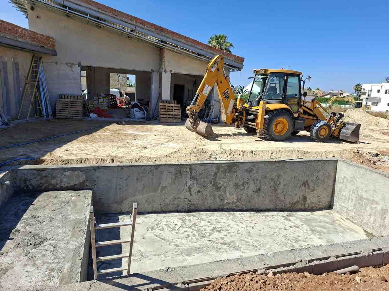 Una retroexcavadora nivela la tierra junto a una base de hormigón en construcción al lado de una casa.