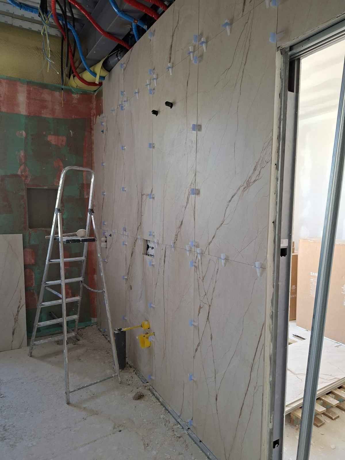 Pared interior parcialmente terminada con cableado expuesto, una escalera y escombros de construcción cerca de una puerta.