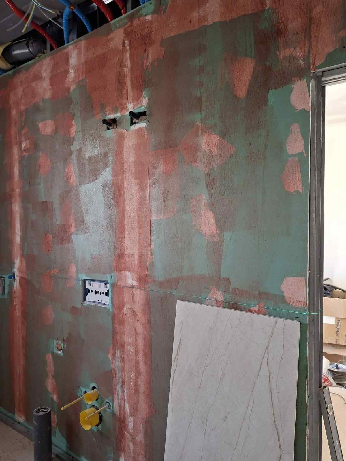 Pared de pladur expuesta con yeso reparado, agujeros y cableado eléctrico visible en una zona de reformas.