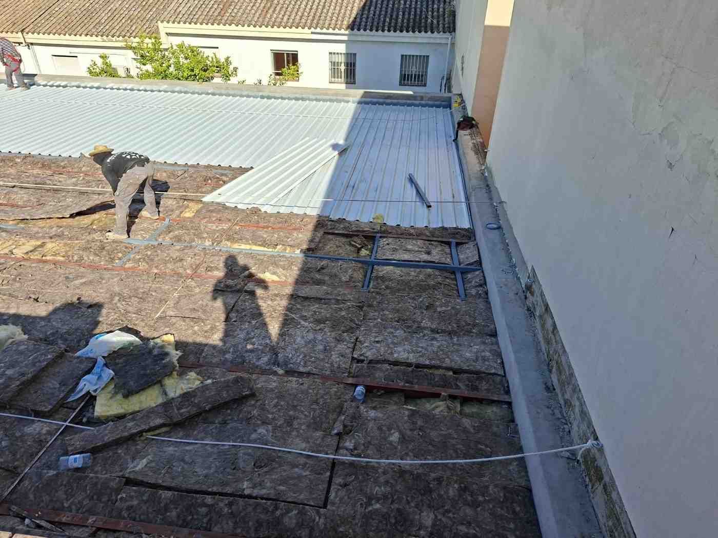 Azotea con grava, trabajadores y una gran sombra cerca de una pared blanca y paneles solares.