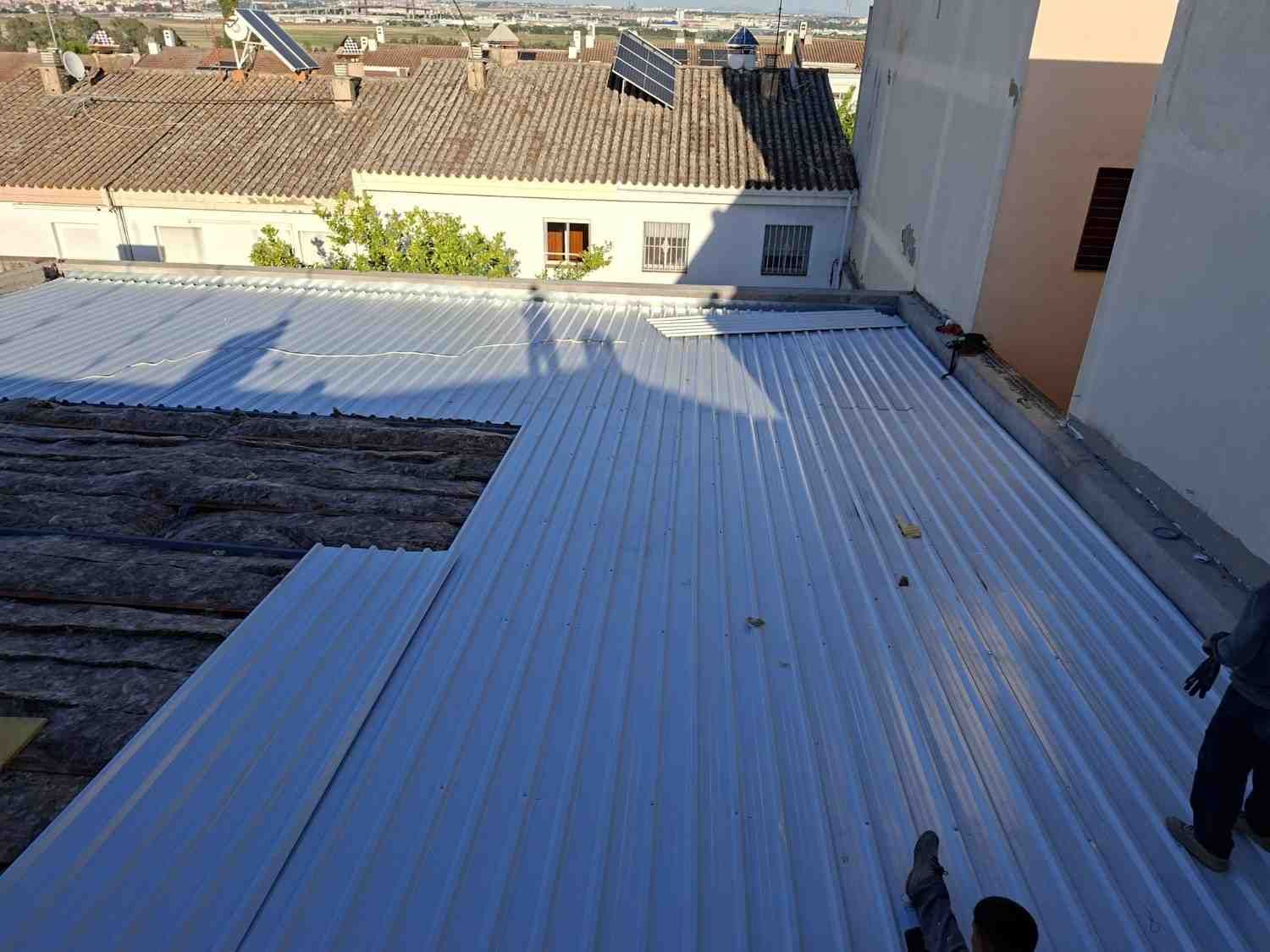 Azotea con techo de chapa ondulada y un trabajador de pie cerca del borde, con vistas a las casas cercanas.