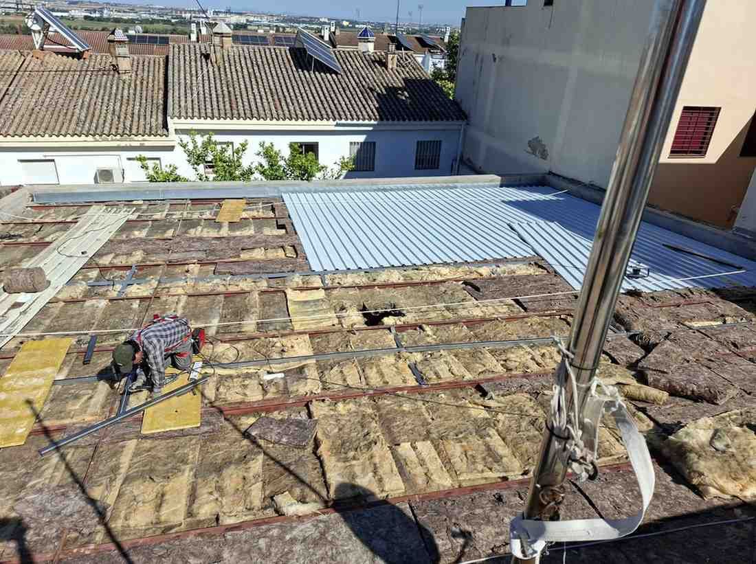 Azotea en reparación con aislamiento expuesto, una lámina de metal corrugado y edificios de la ciudad al fondo.