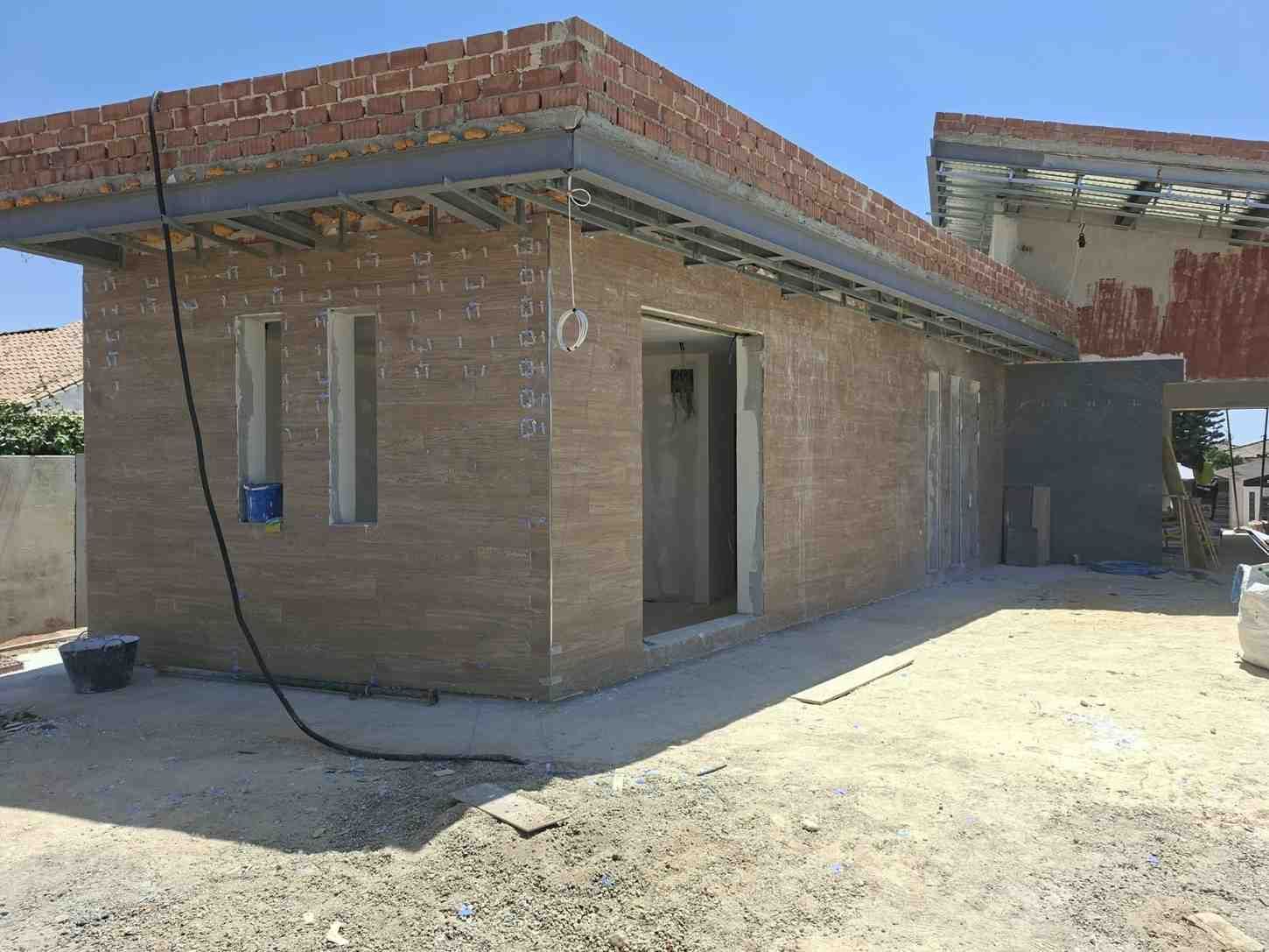 Casa de ladrillo en construcción con andamios metálicos y techo sin terminar a plena luz del día.