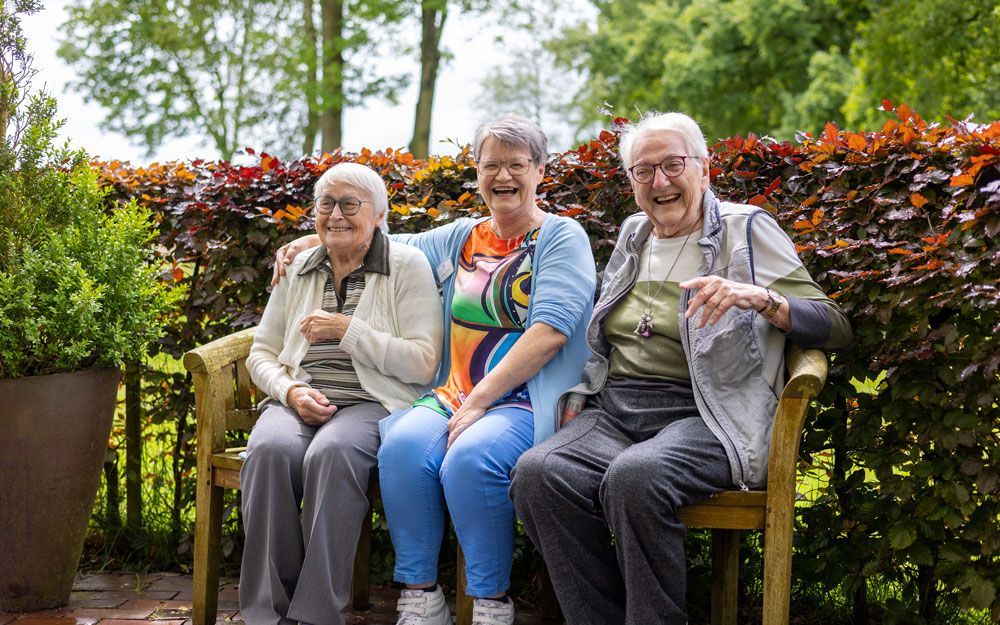 Drei ältere Menschen sitzen auf einer Bank in einem Park.