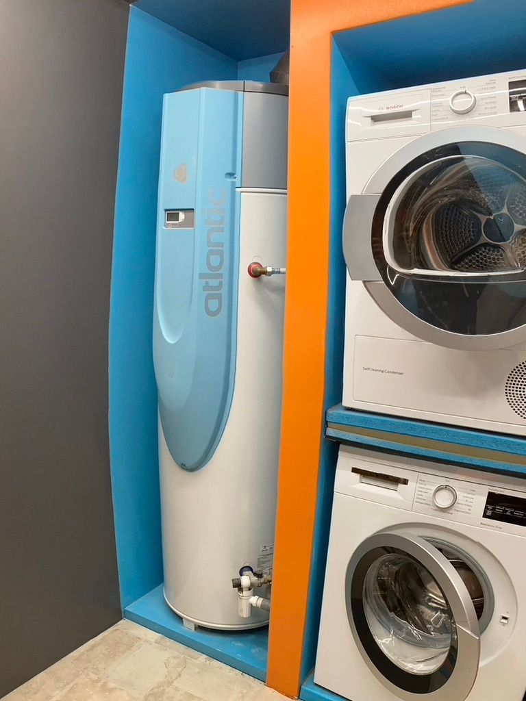 Chauffe-eau à côté d'une laveuse et d'une sécheuse superposée dans un placard de rangement.