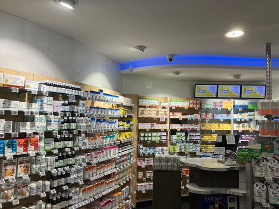 Intérieur lumineux d'une pharmacie avec des étagères de médicaments, un comptoir et des lumières au plafond.