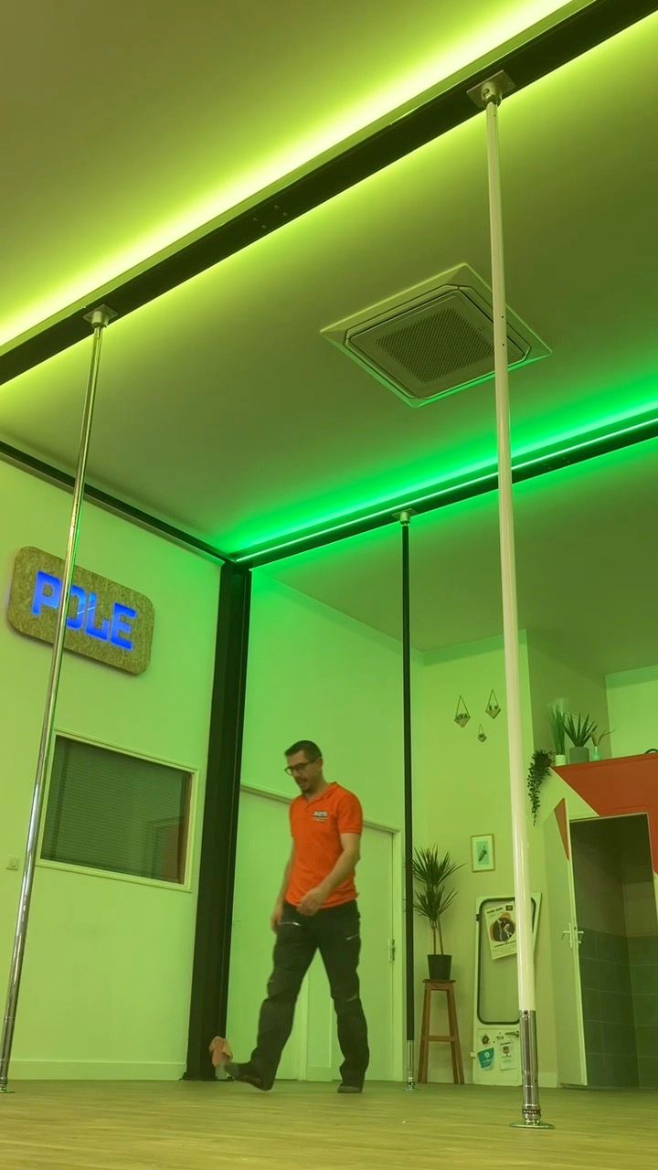 Un homme en chemise se tient debout dans une pièce éclairée, avec des poteaux.