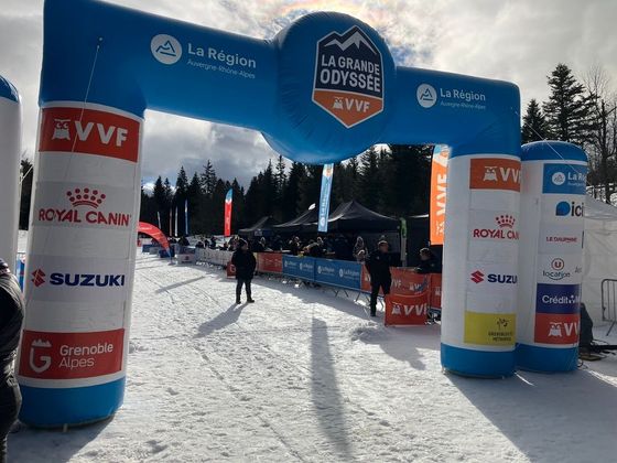 Arche d'arrivée extérieure enneigée avec banderoles de sponsors et personnes marchant.
